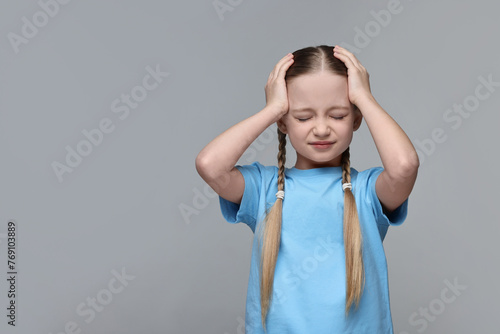Little girl suffering from headache on grey background. Space for text