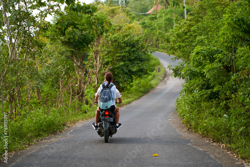 A person on a motorcycle rides a scenic asphalt road in Asia.