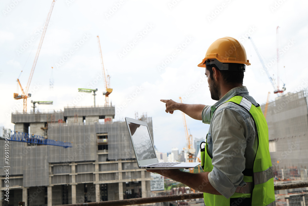 A project engineer at a construction site holds a laptop to track progress according to the plan. Monitoring progress is key to success. Our project engineer is on-site, armed with a laptop to ensure A project engineer at a construction site holds a laptop to track progress according to the plan. Monitoring progress is key to success. Our project engineer is on-site, armed with a laptop to ensure