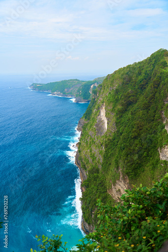 A panorama of a massive green cliff overhanging the stormy ocean.