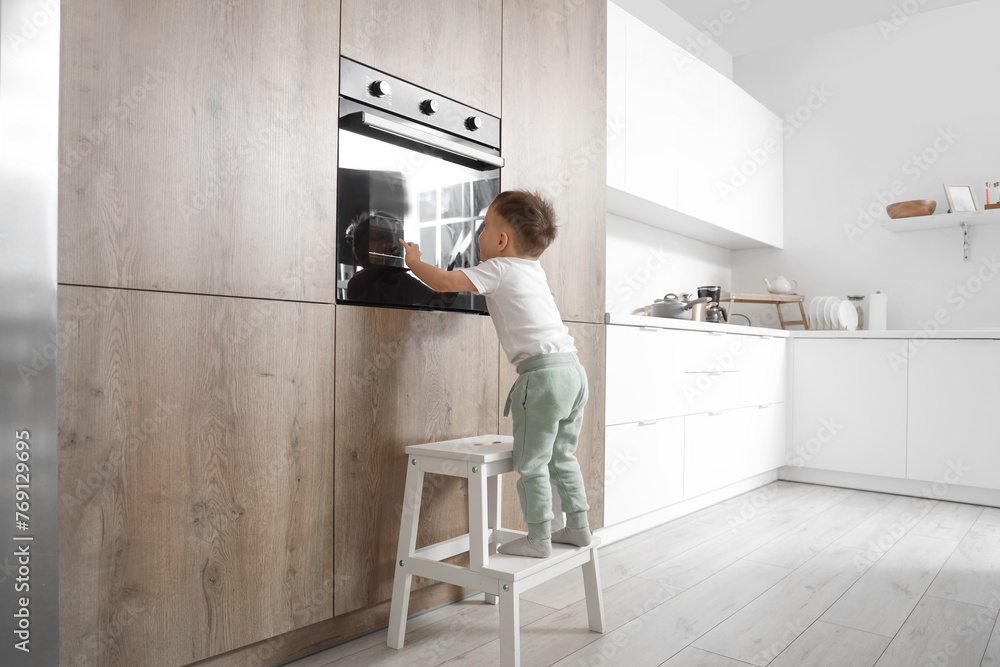 Little boy climbing on step stool near oven in kitchen. Child at risk Little boy climbing on step stool near oven in kitchen. Child at risk