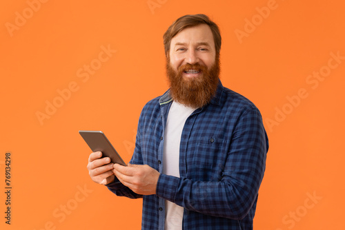 Cheerful redhaired bearded man in casual holding digital tablet, studio