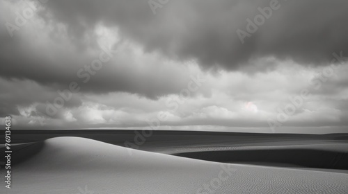 a black and white photo of a vast expanse of sand dunes under a cloudy sky with a sun in the distance. photo