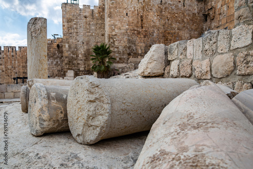 Dramatic image of ruins in front of the old city Jerusalem gates with weathered stone columns in the foreground.