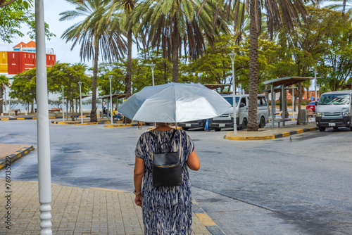 On a hot sunny day, a woman stands under a UV umbrella at the bus station in downtown Willemstad, Curacao.
