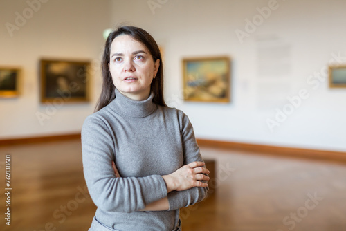 Positive brunette admiring artworks at paintings exposition walking in spacious museum hall.. photo