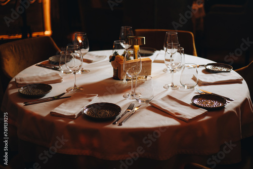Beautifully organized event - round served table banquet ready for guests, round decorated table with empty plate, glasses, forks, napkin. Elegant dinner table 