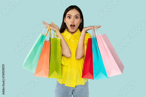 Excited surprised young woman with shopping bags at blue backgtound