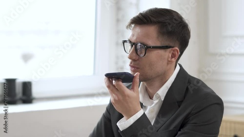 A man dictating a voice message uses a phone and a voice assistant. photo