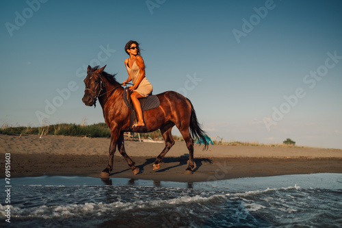 A young woman is riding a horse on a seaside beach at summer.
