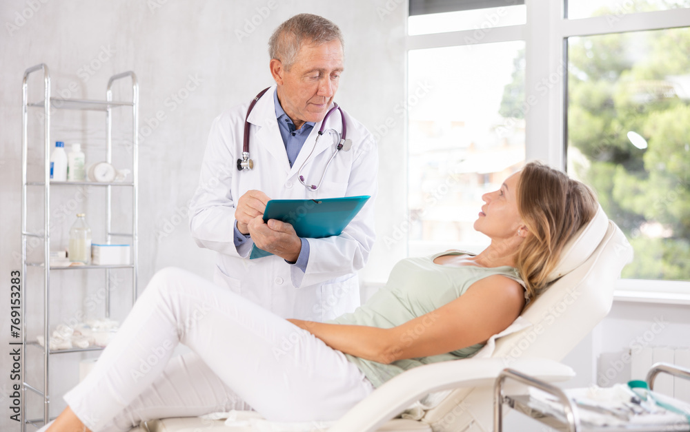 Fototapeta premium Male senior doctor conducts survey of female patient after procedure and fill in data in client medical record
