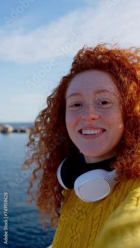 Young happy redhead woman talking to camera. Teenager influencer live streaming outdoors. Tourist having video call.