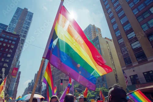 A rainbow flag waving in the wind at an outdoor pride event, with other flags and people celebrating around it against city buildings in background Generative AI photo