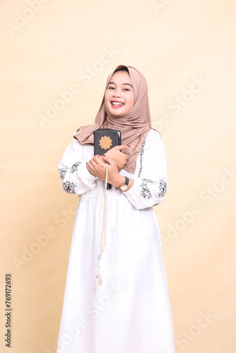 Beautiful mature Asian Muslim girl wearing a right-slanted hijab, smiling cheerfully, holding a quran and holding prayer beads. for advertising, lifestyle, banners and Ramadan