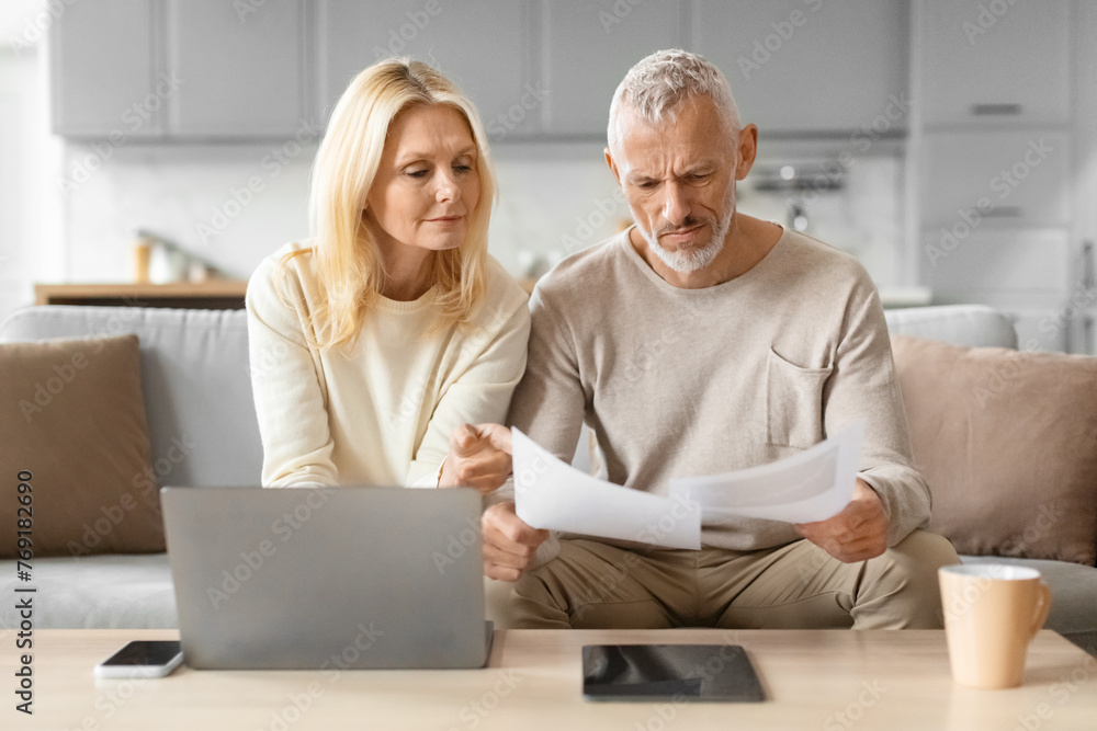 Focused couple looking at documents by a laptop Focused couple looking at documents by a laptop