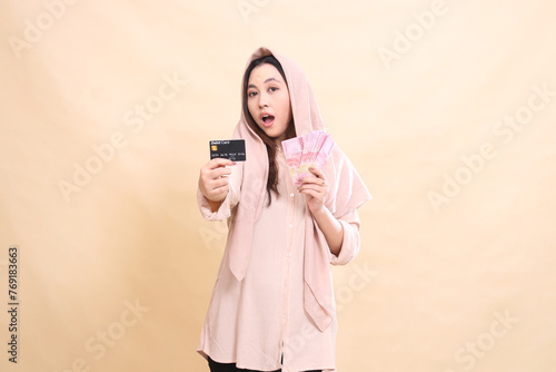 girl Asian expresses surprise at you, hands holding debit card forward and carrying rupiah money. young beautiful for finance, advertising, fashion
