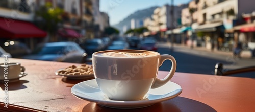 Fototapeta Naklejka Na Ścianę i Meble -  White cup of coffee on table in outdoors cafe with blurred city street background, Morning coffe