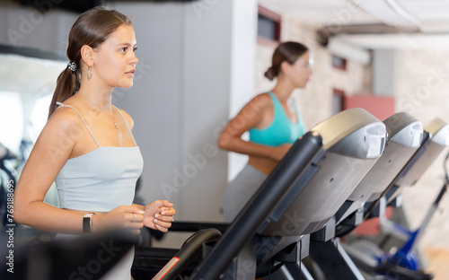 Girl walk on treadmill in gym. Active hobby, healthy lifestyle, extensive training. Happy sporty people interacting in weight room training - social gathering concept in sport lifestyle context