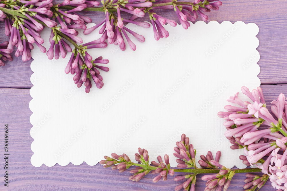Lilac branch and empty white card on lilac wooden surface