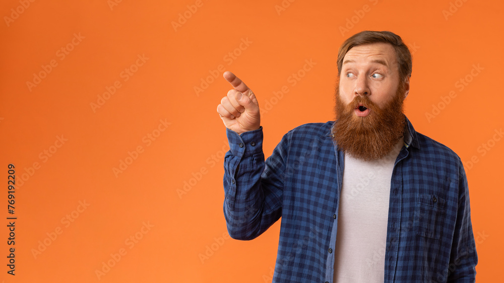 Fototapeta premium Amazed Redhaired Man Pointing Finger Aside At Empty Space, Studio