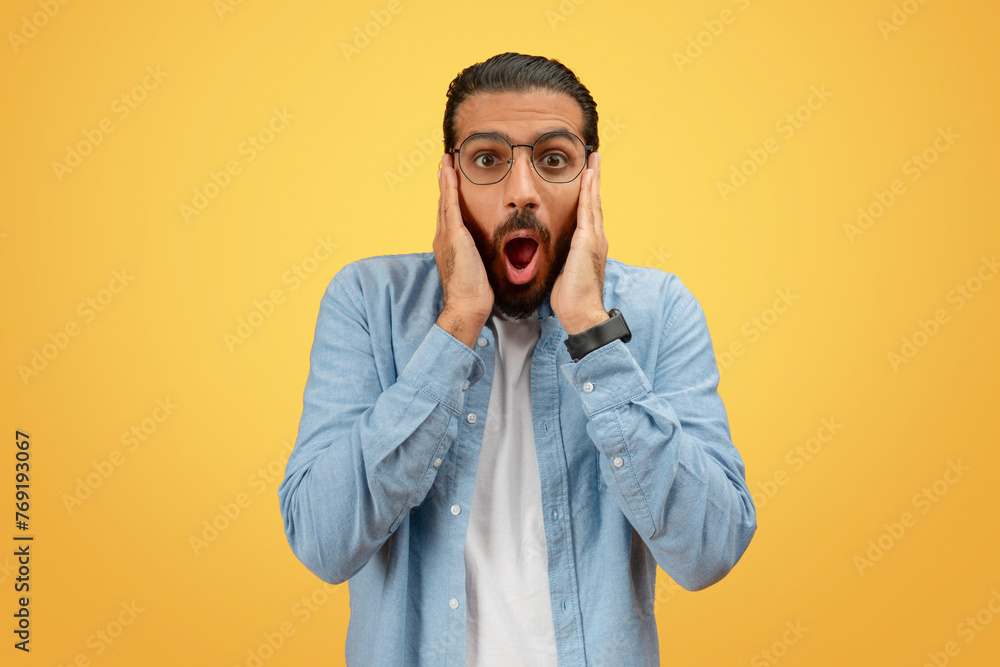 Shocked man with hands on cheeks on yellow Shocked man with hands on cheeks on yellow