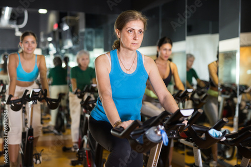 Portrait of confident adult woman training on fitness bike in gym indoor