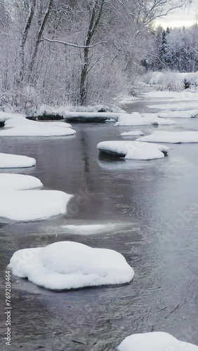 The rocks that is covered with white snow in the river. Further afield, forest and winter landscape. The camera glides slowly backwards low over the water. Geology shot. Vertical Format Video photo