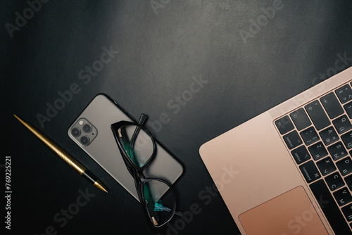 Business layout with items for design. Phone, glasses, pen, laptop on the table. In a dark style, there are object layouts on the table. Top view of items
