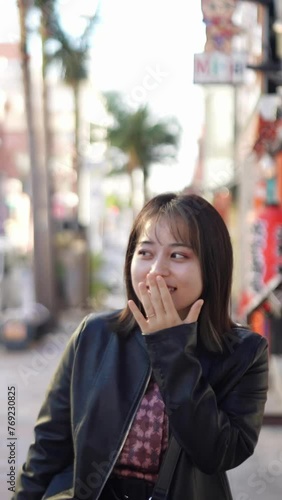 Slow-motion vertical video of a young Japanese woman from Okinawa Prefecture in her 20s walking with a smile on Kokusai Street in Naha City, Okinawa Prefecture 沖縄県那覇市の国際通りで笑顔で歩く20代の沖縄県出身の若い日本人女性のスローモー photo