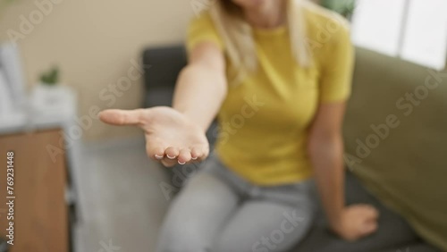 Attractive young blonde woman in a t shirt, cheerfully offering her empty palm hand, embodying the concept of giving assistance and acceptance in cozy home interior. photo