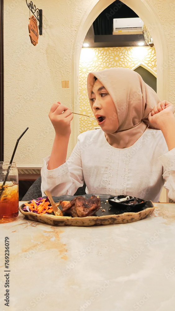 candid portrait of beautiful asian woman eating on potatoes, khubus (pita bread) and oven roasted chicken typical arabic food with fork and knife on plate inside restaurant candid portrait of beautiful asian woman eating on potatoes, khubus (pita bread) and oven roasted chicken typical arabic food with fork and knife on plate inside restaurant