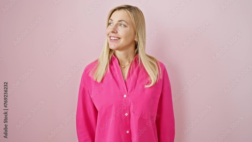 Confident young blonde woman relaxing in casual, natural pose, looking away with a content smile. standing in profile over pink isolated background. Confident young blonde woman relaxing in casual, natural pose, looking away with a content smile. standing in profile over pink isolated background.