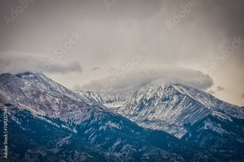 Powerful image of towering mountains with snowy peaks enveloped by a dramatic, cloudy sky suggesting change © chad