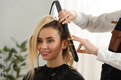 Hair styling. Hairdresser curling woman s hair in salon  closeup