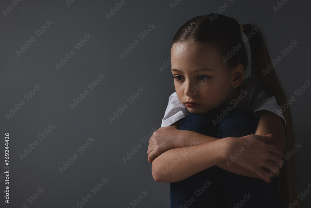 Sad girl sitting near dark grey background, space for text Sad girl sitting near dark grey background, space for text