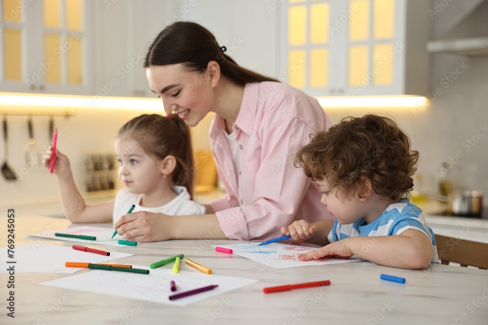 Mother and her little children drawing with colorful markers at table in kitchen Mother and her little children drawing with colorful markers at table in kitchen