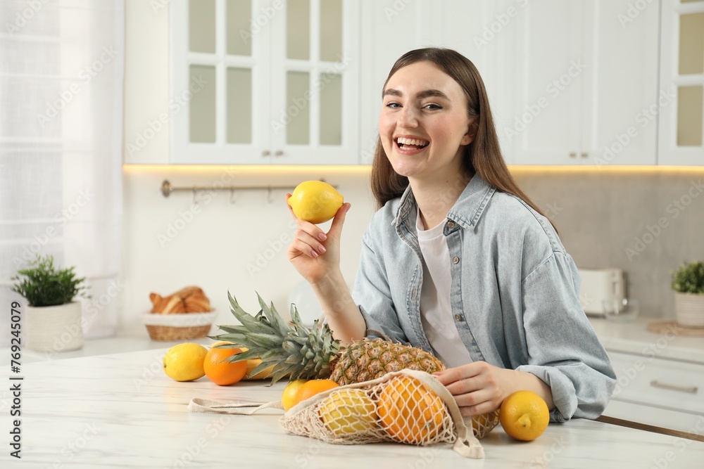 Obraz premium Woman with lemon and string bag of fresh fruits at light marble table in kitchen