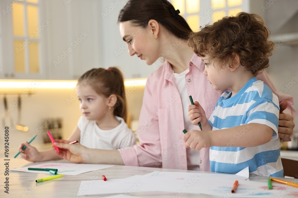 Mother and her little children drawing with colorful markers at table in kitchen Mother and her little children drawing with colorful markers at table in kitchen