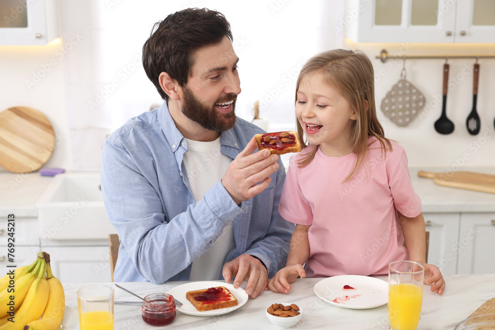 Father and his cute little daughter having breakfast at table in kitchen Father and his cute little daughter having breakfast at table in kitchen