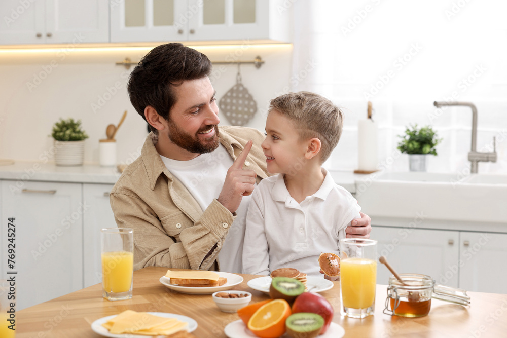 Father and his cute little son having fun during breakfast at table in kitchen