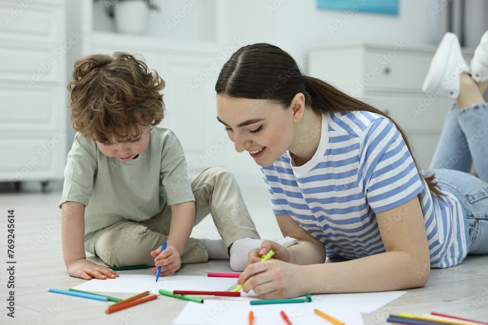 Mother and her little son drawing with colorful markers on floor at home Mother and her little son drawing with colorful markers on floor at home