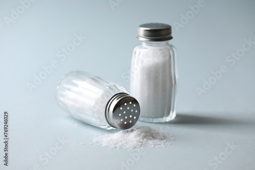 Natural salt in shakers on color background