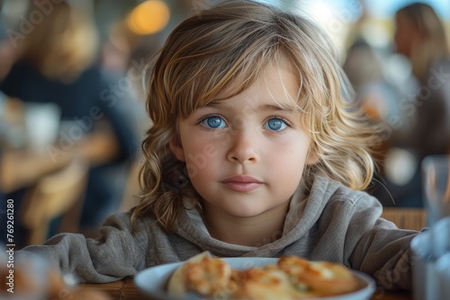 Young child with striking blue eyes gazes while sitting at a restaurant table with food