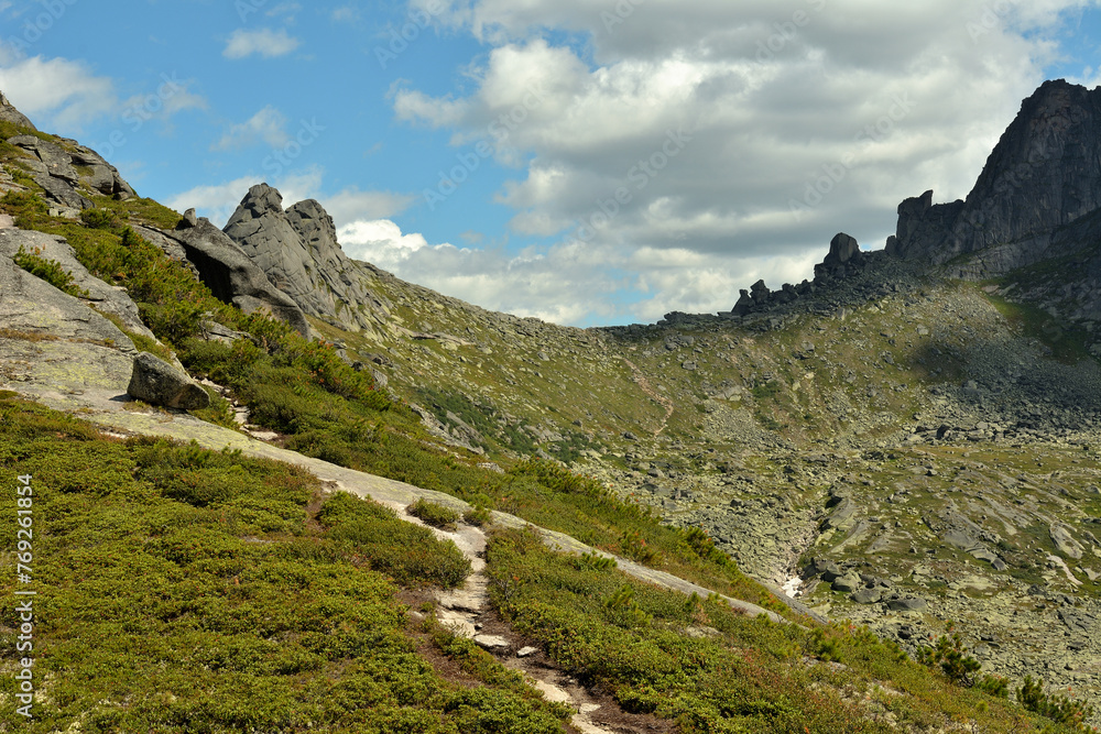 Obraz premium Crossroads of hiking trails on the slope of a high mountain overlooking the pass under a cloudy summer sky.