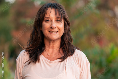 Beautiful senior woman 50 to 60 years old posing in casual clothes, smiling in an outdoor park at sunset