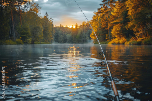 The tip of a fishing rod captures the last light as it reflects off a calm forest-lined lake at sunset photo