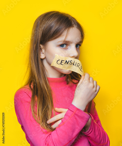 A child with his mouth taped peels off a piece of tape with the words "CENSURE" written on it. Yellow background. Ban on opinion, unwillingness to listen to children, restriction of freedom of speech.