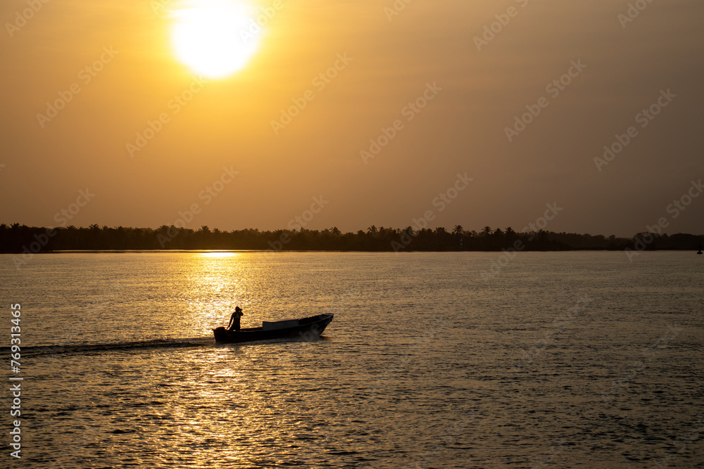Silhouette of a fisherman in a boat on the river at sunset
