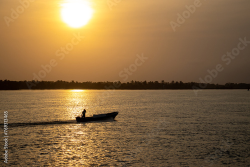 Silhouette of a fisherman in a boat on the river at sunset