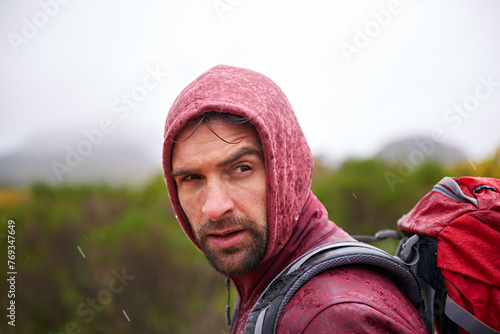Man, mountain and hiking in rain for fitness, wellness and exercise for training and adventure in environment. Young person with backpack and rock for workout and trekking in morning with weather